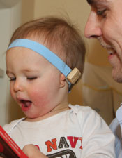 Young child on parent's lap wearing a Baha bone conduction hearing aid
