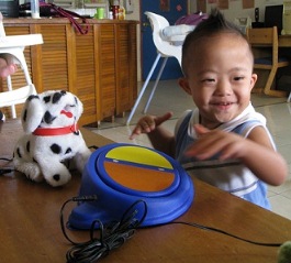Boy standing by a simple switch that operates a toy dog facing towards camera