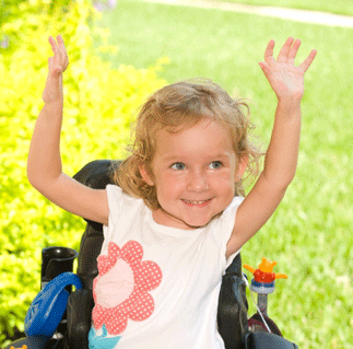 Child with spinal muscular atrophy in wheelchair, raising arms in the air, smiling