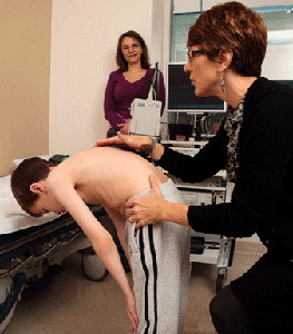 Boy leaning over while medical provider checks spine and a woman looks on